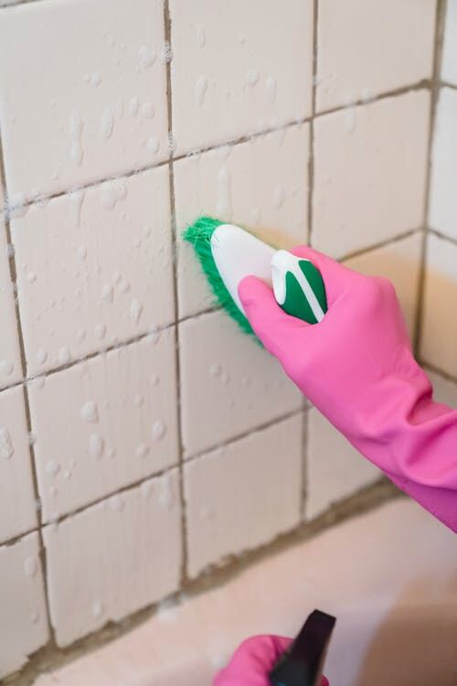 A homeowner attempting to scrub grout lines in a tiled bathroom.