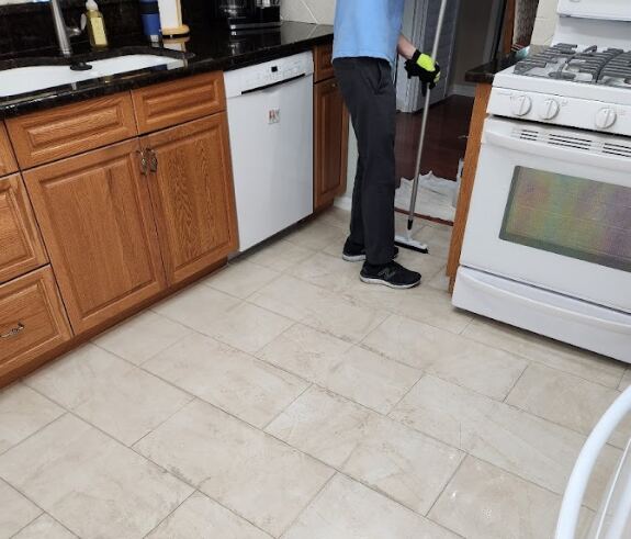 The image shows a person cleaning the kitchen floor with a mop, near the stove and dishwasher.