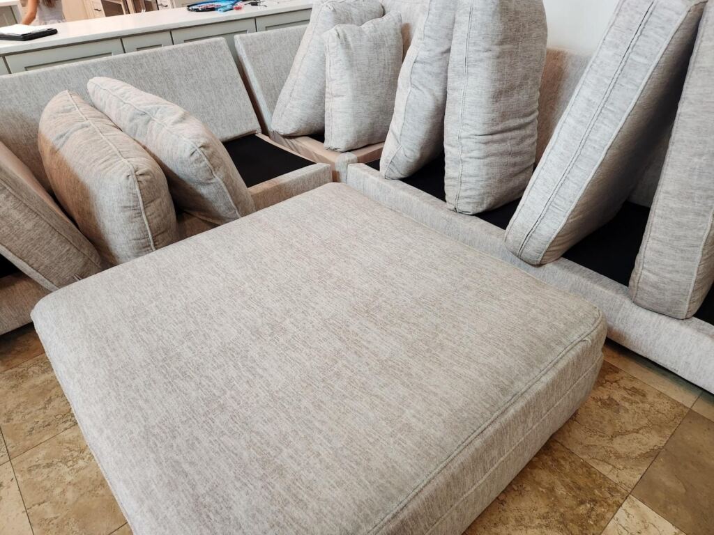 A sectional sofa with light gray cushions is shown with all the cushions removed or propped up, likely in preparation for cleaning or maintenance.