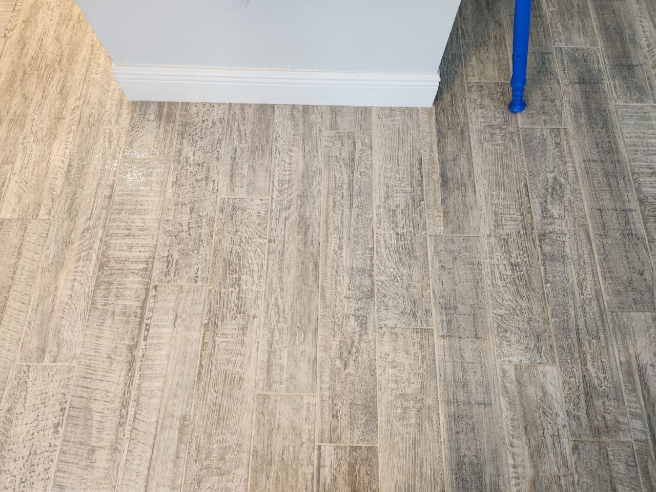 A section of wood-look tile flooring shows a clear contrast between the freshly cleaned lighter area on the left and the darker, still-dirty section on the right.