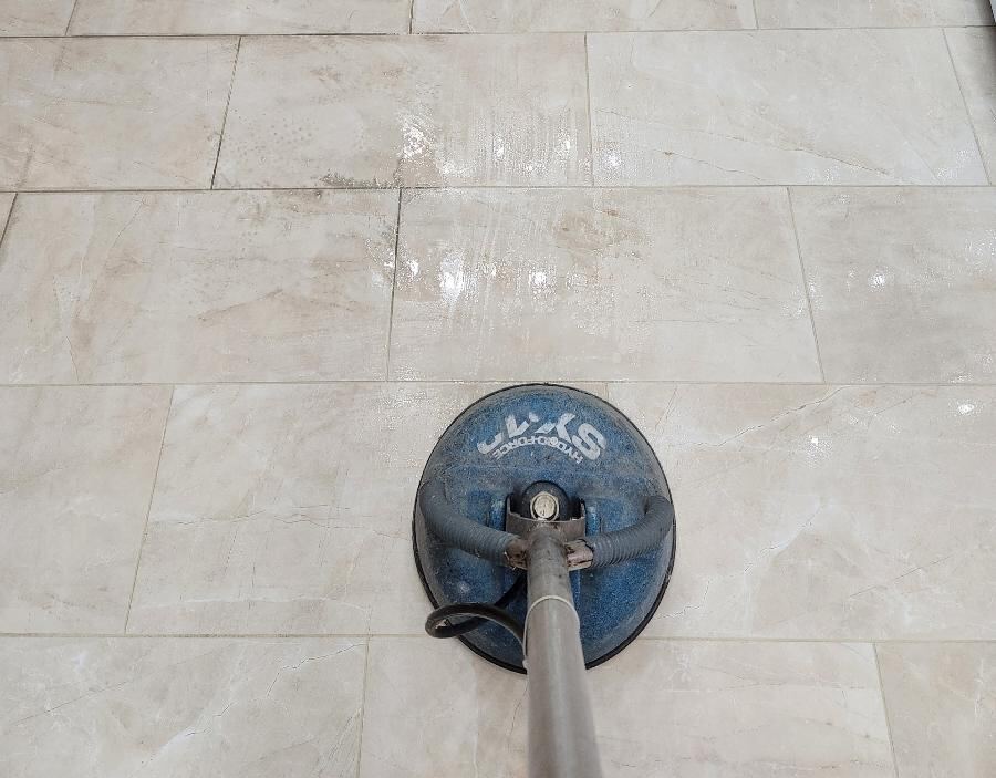The image shows a tile floor being cleaned with a floor cleaning machine.