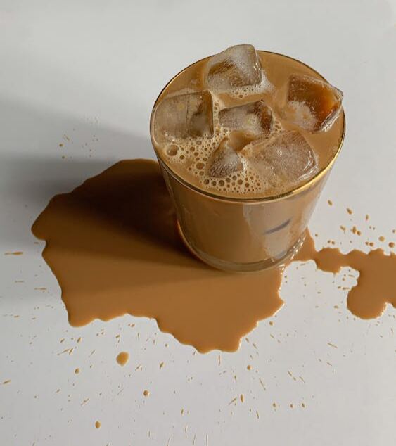 A glass of iced coffee with spilled coffee on the surface.