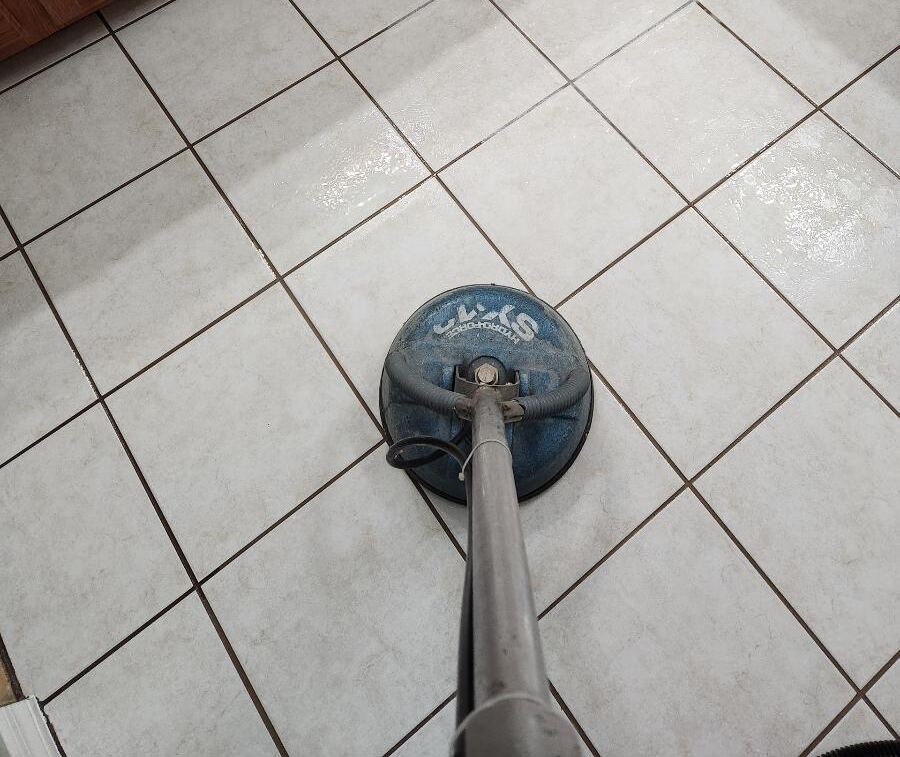 A floor cleaning machine is being used on tiled kitchen floors with wooden cabinets in the background.