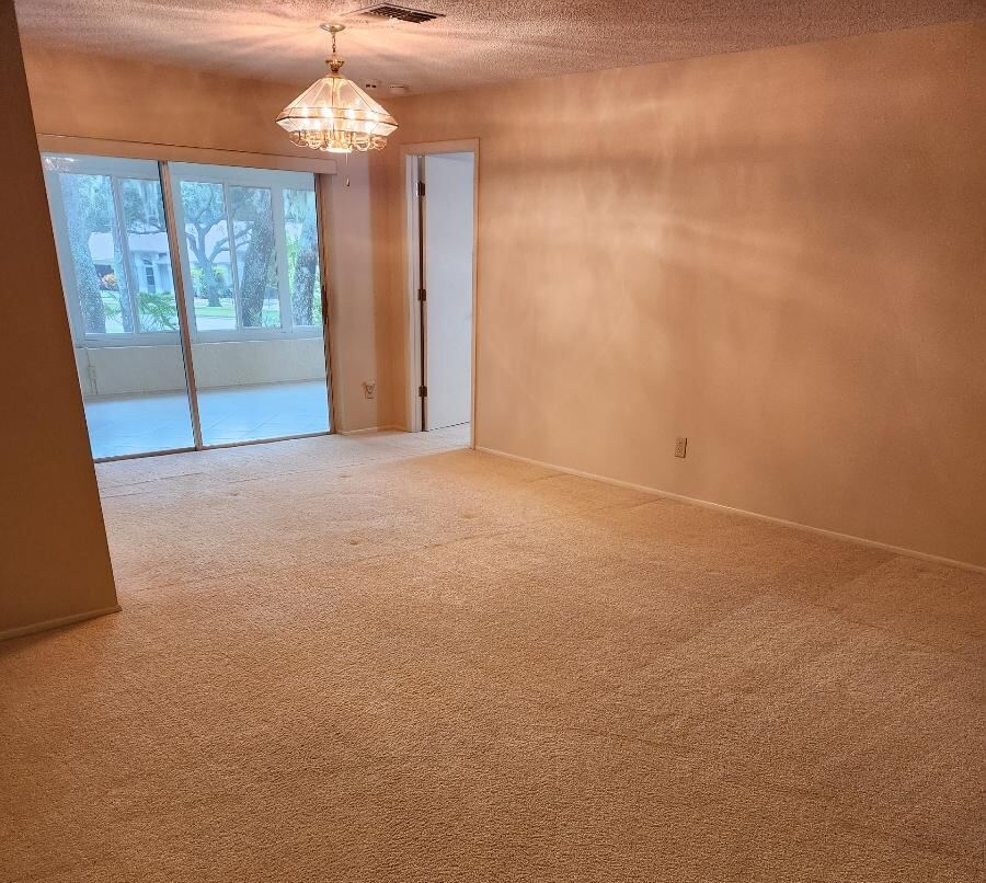 Empty, carpeted living room with a chandelier and sliding glass door to the outside.