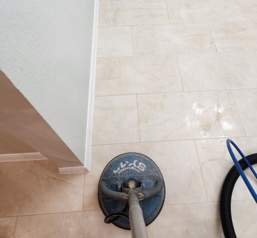 Tile floor being cleaned with a floor buffer, showing some moisture and the edge of the room.