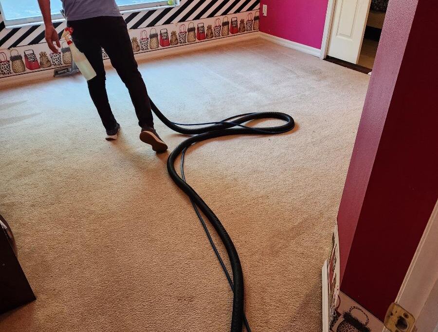 A person is using a vacuum hose while cleaning a carpeted room.