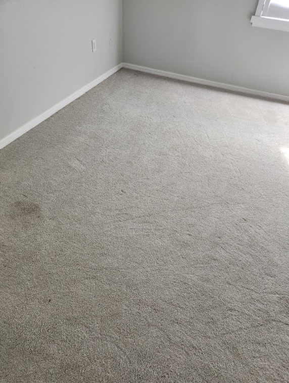 Light-colored bedroom carpet with visible stains and dirt spots before professional cleaning