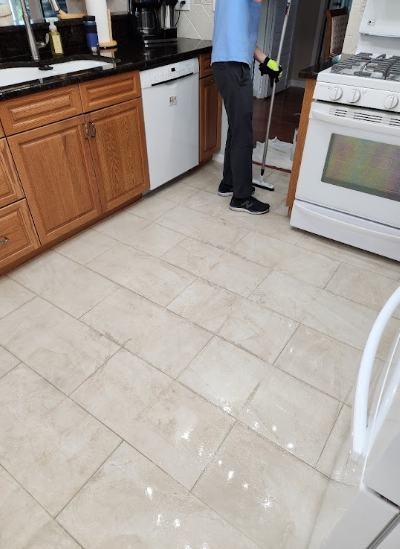 Person steam mopping tiled kitchen floor with visible moisture and shine